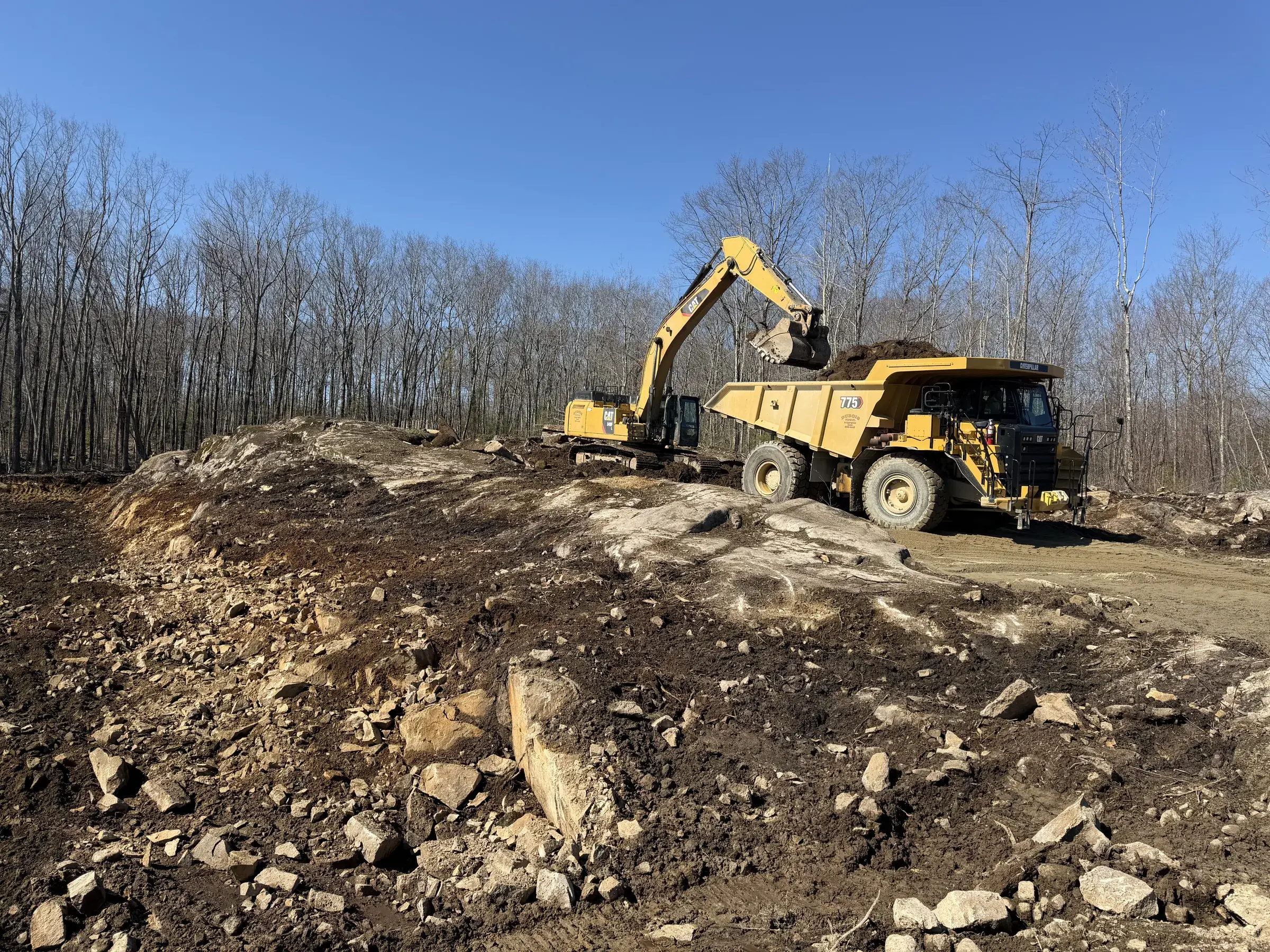 Excavator loading topsoil into a Dubois dump truck